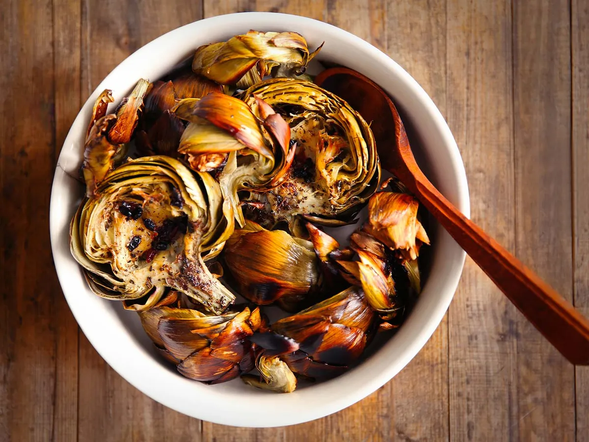 Bol en faïence contenant des fonds d'artichaut braisés, nappés d'une sauce claire aux herbes et citron, posé sur une planche en bois