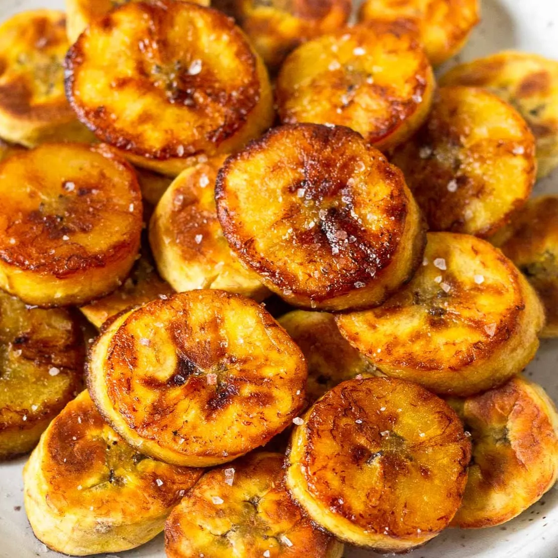 Tranches de banane plantain rôties au caramel, nappées d'un beurre salé brillant, servies sur une assiette blanche