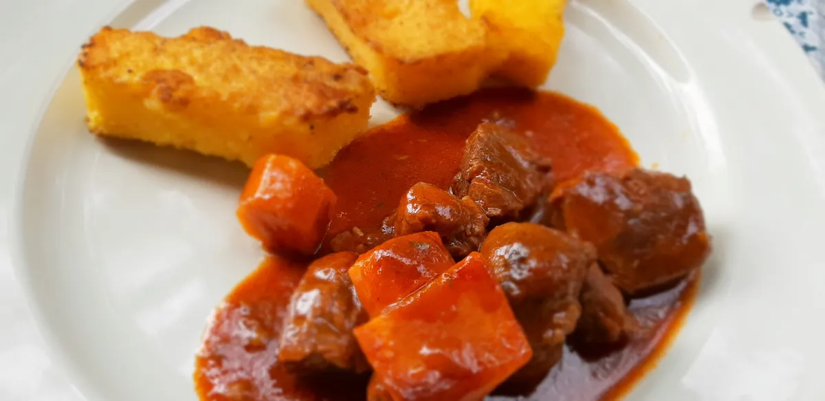 Cocotte en fonte ouverte avec des joues de porc braisées dans un jus brun, carottes et oignons dorés autour de la viande