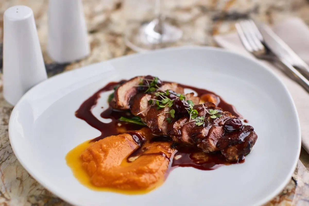 Tranches de magret de canard rosées, nappées d'une sauce brillante, accompagnées de quartiers d'orange et d'herbes fraîches.