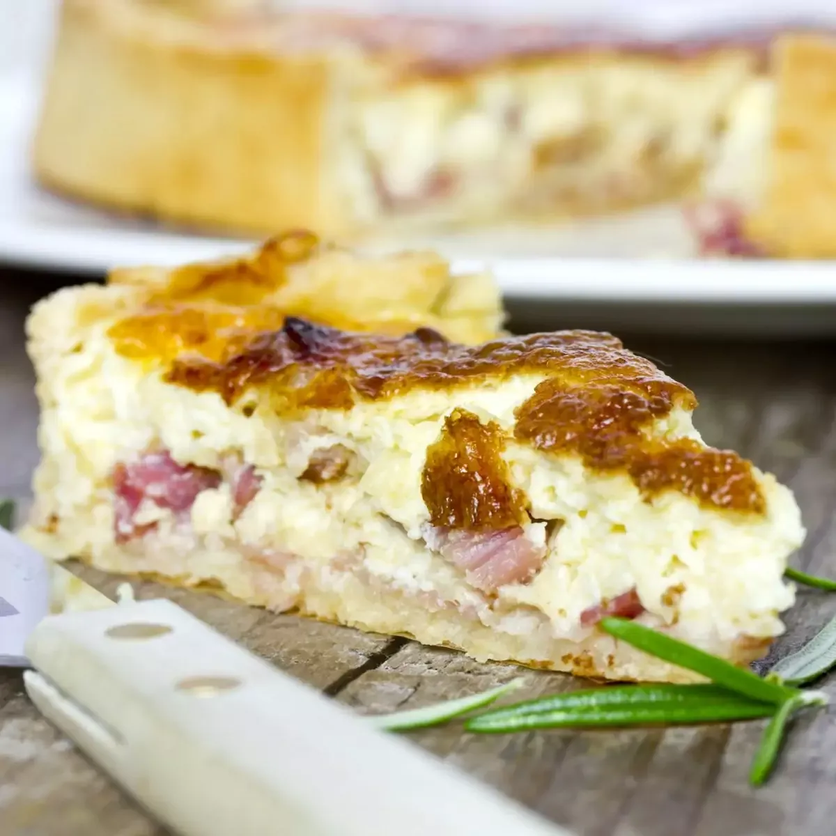 Quiche lorraine tranchée sur assiette en porcelaine, pâte dorée et appareil crémeux parsemé de lardons croustillants
